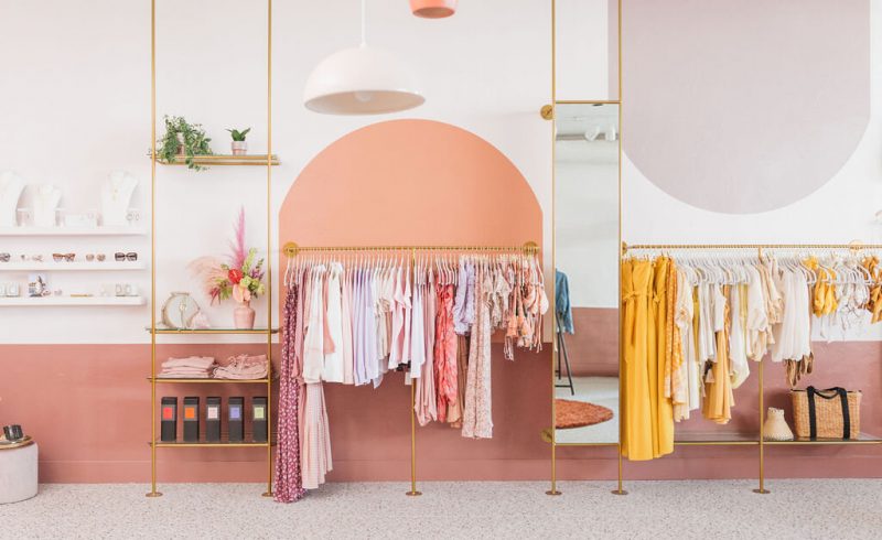 vêtements de couleurs sur portants en métal doré dans une boutique aux murs roses et saumon
