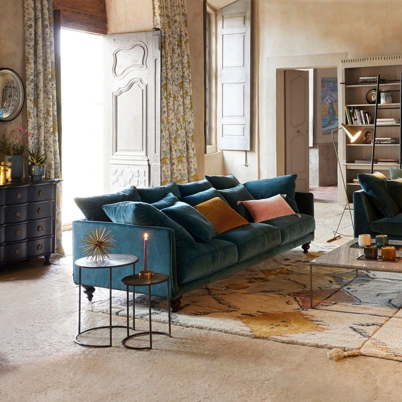 large canapé en velours de couleur vert émeraude dans un grand salon au rideaux fleuris