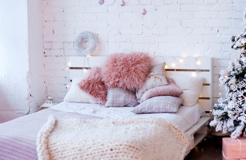 tête de lit en palette blanche avec des coussins roses sur le lit et une guirlande lumineuse dessus