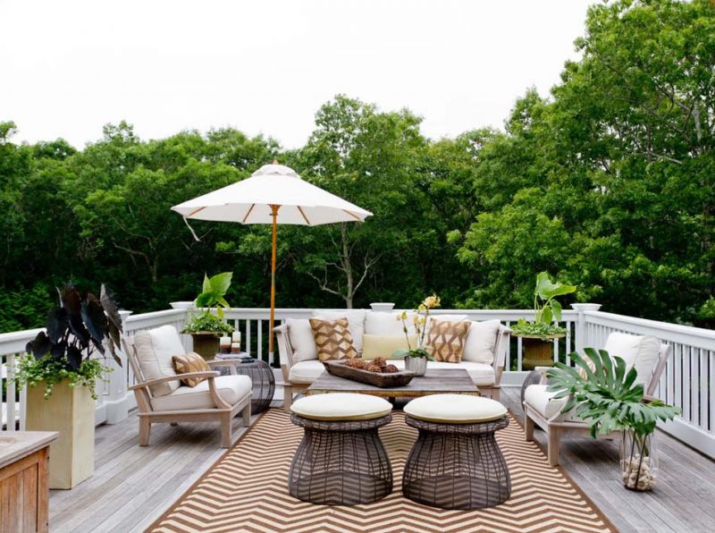 Une grande terrasse avec vue sur la nature, un tapis graphique et un salon de jardin en bois