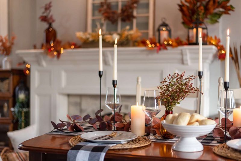 Une table avec de la déco Thanksgiving réalisée avec des bouquets de feuilles séchées et des bougies