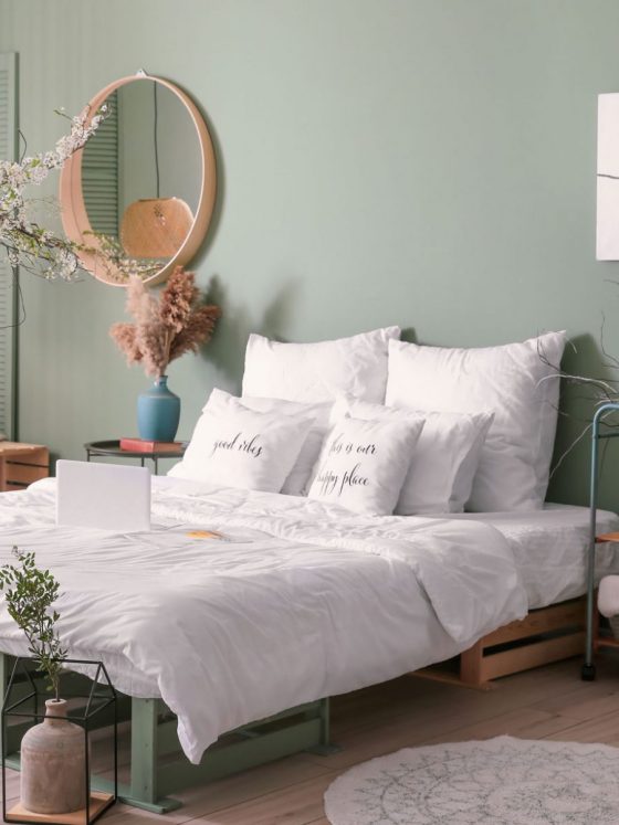 Une déco chambre tendance avec des murs vert amande, un lit blanc et des accessoires en osier