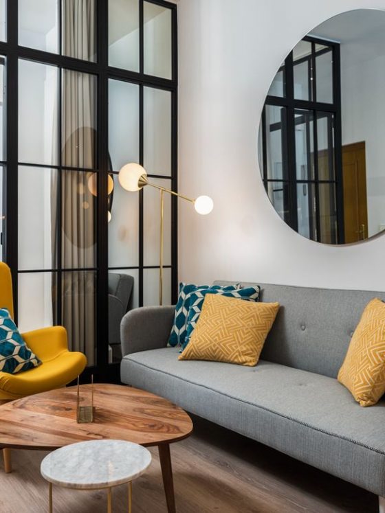 Un salon de style scandinave, avec une verrière et un grand miroir décoratif mural rond au-dessus du canapé