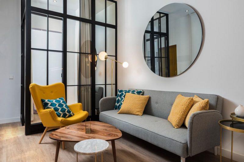 Un salon de style scandinave, avec une verrière et un grand miroir décoratif mural rond au-dessus du canapé