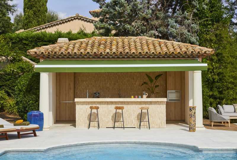 aménagement pool house d'aspect symétrique, avec un espace bar et trois hauts tabourets